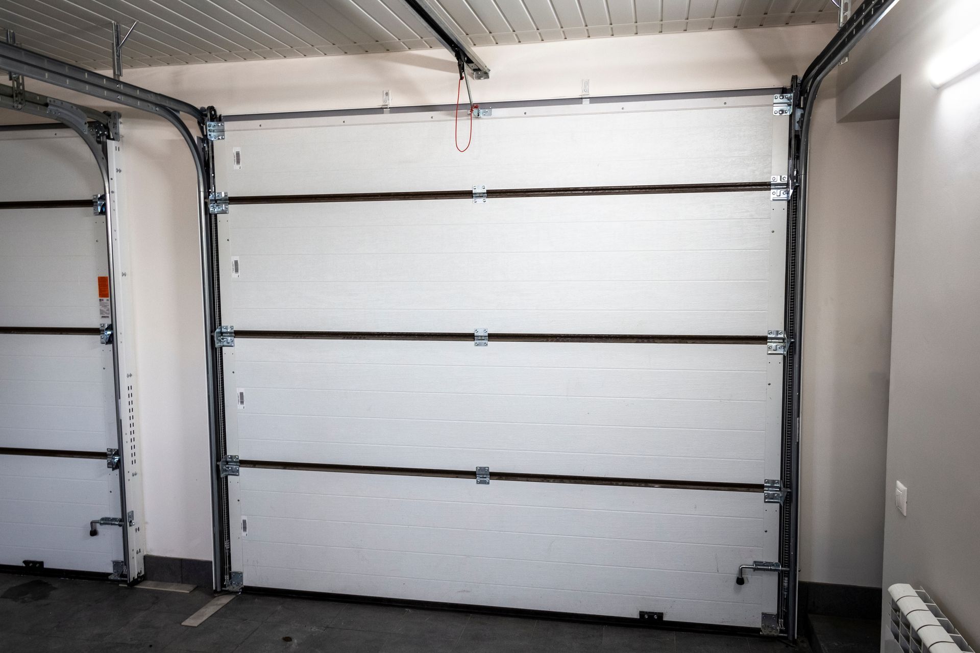Interior view of a closed white garage door with black hinges and a light gray wall