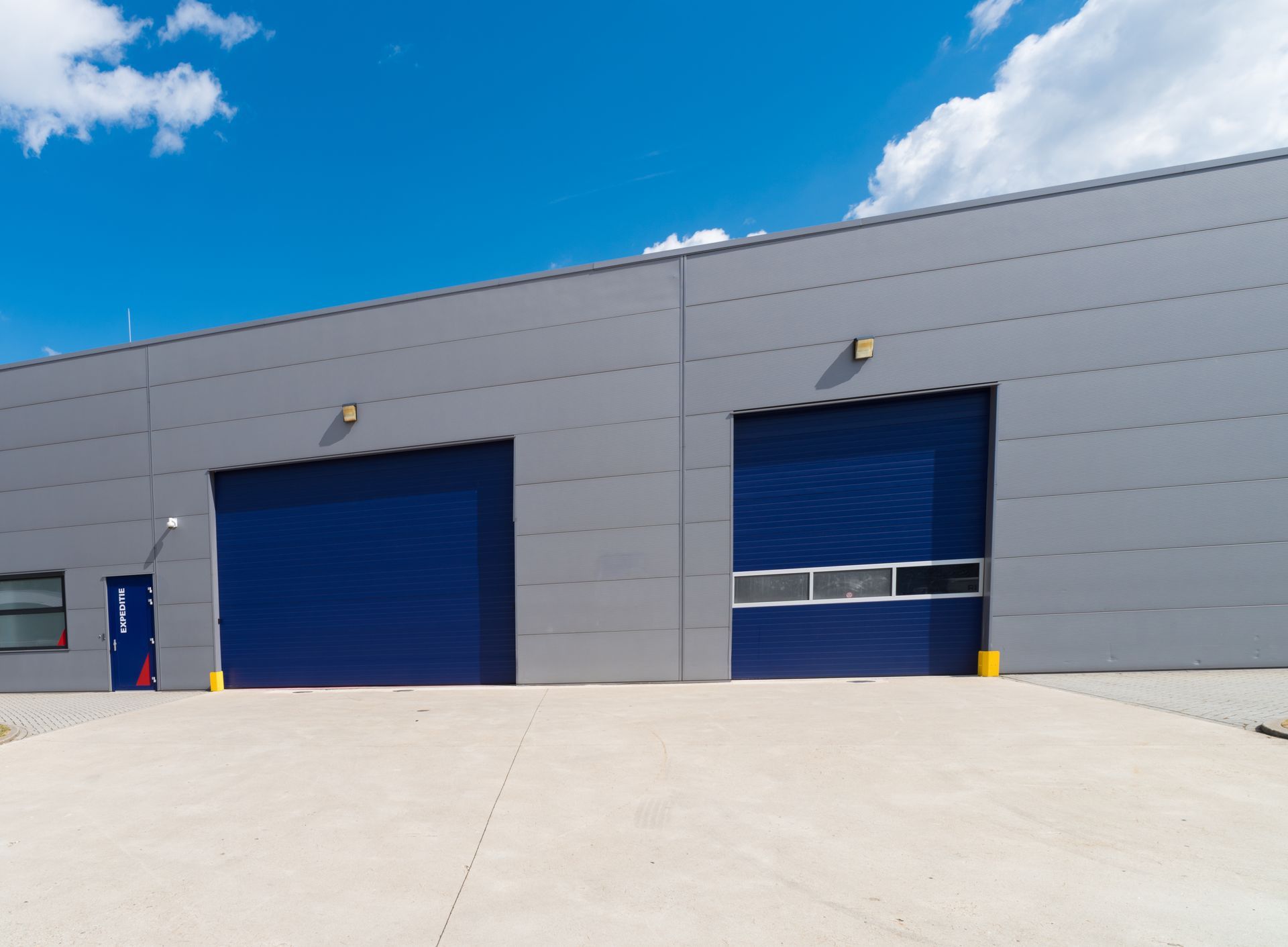 Modern industrial building with two large blue garage doors under a bright blue sky