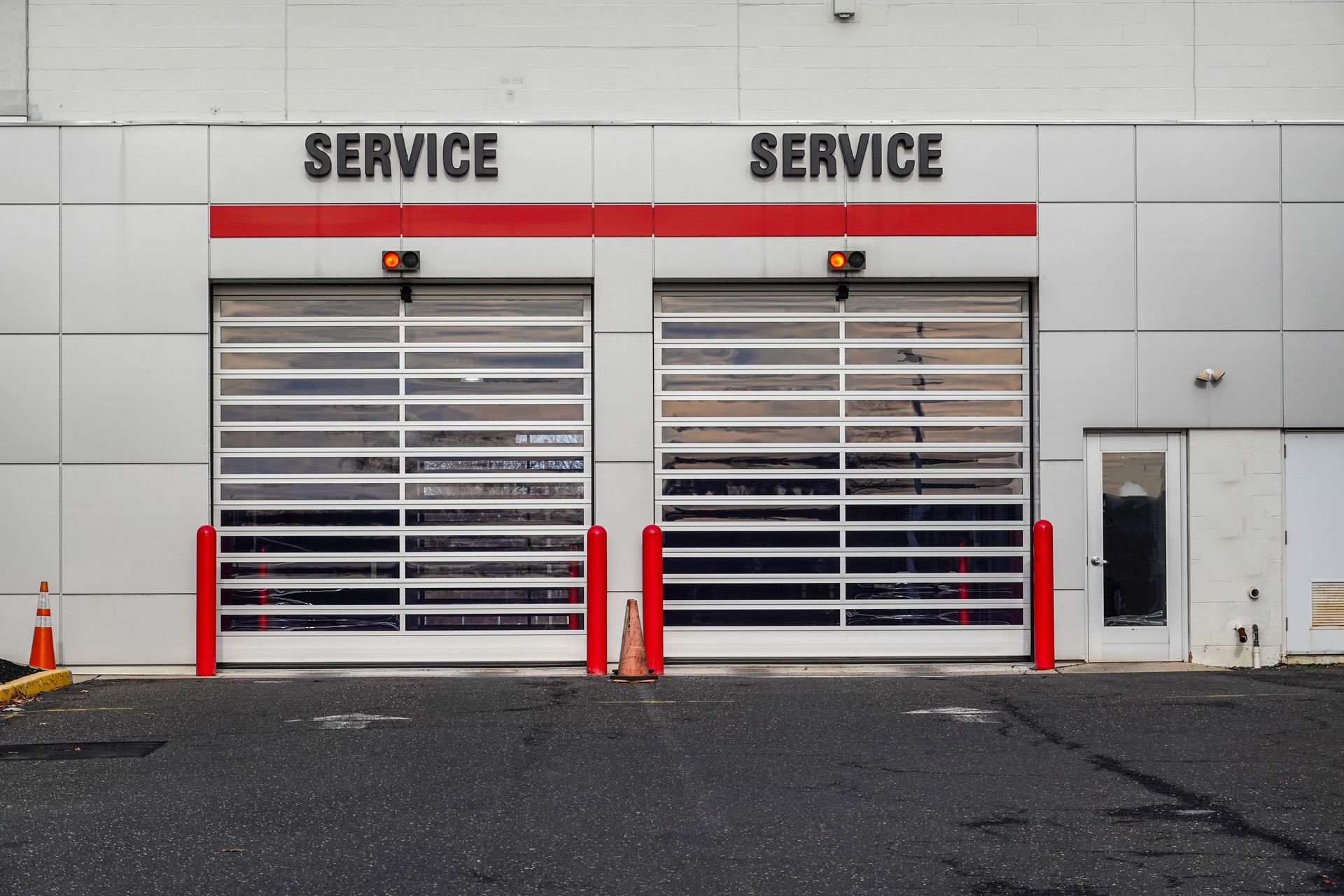 Two white service garage bays with red trim and closed roll-up doors on a paved lot