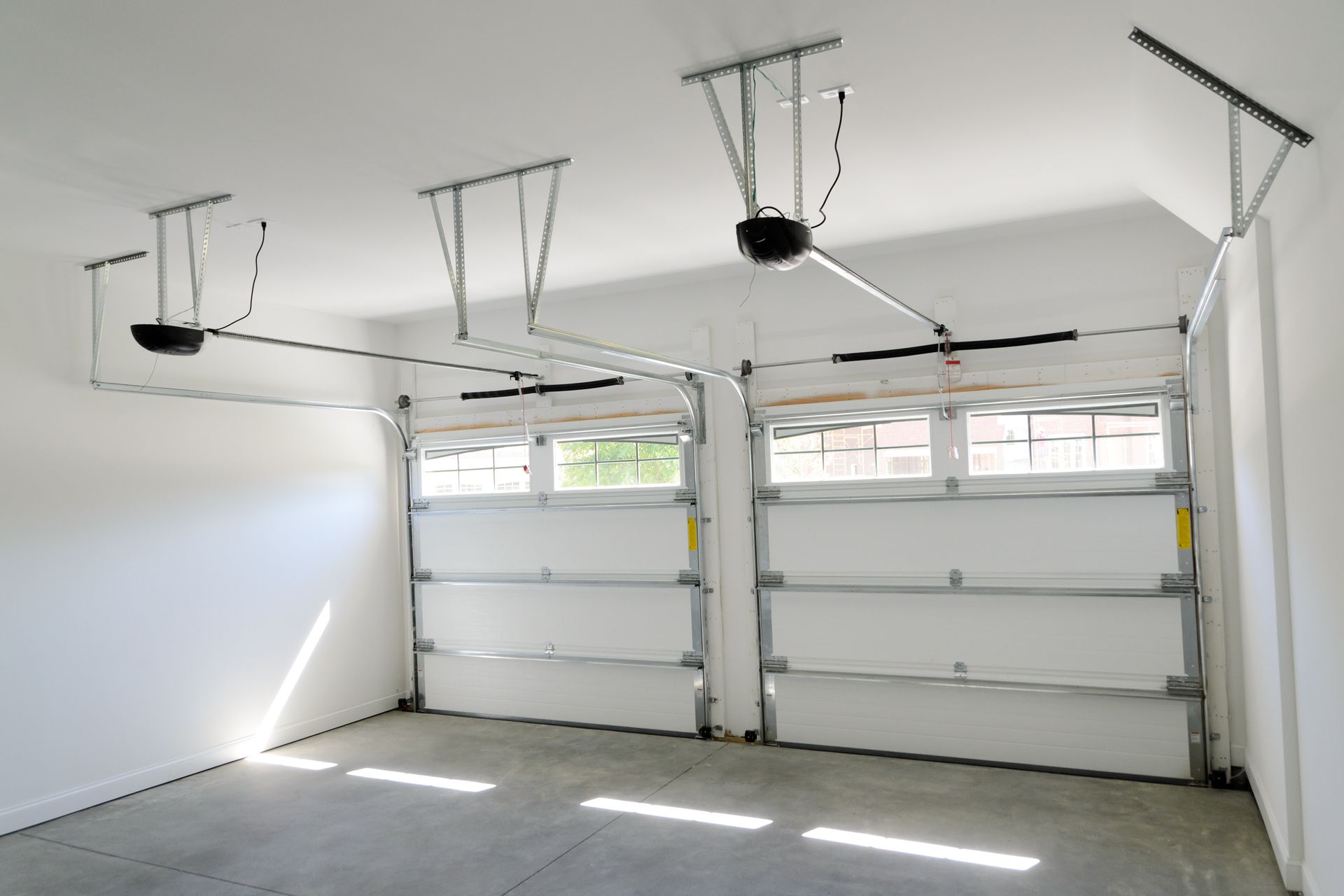 Empty white garage with three overhead doors and ceiling-mounted garage door openers.