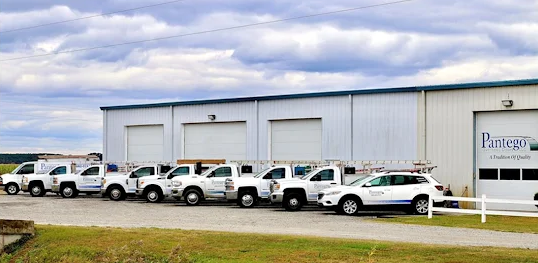 White service vans parked outside a large gray industrial building on a cloudy day