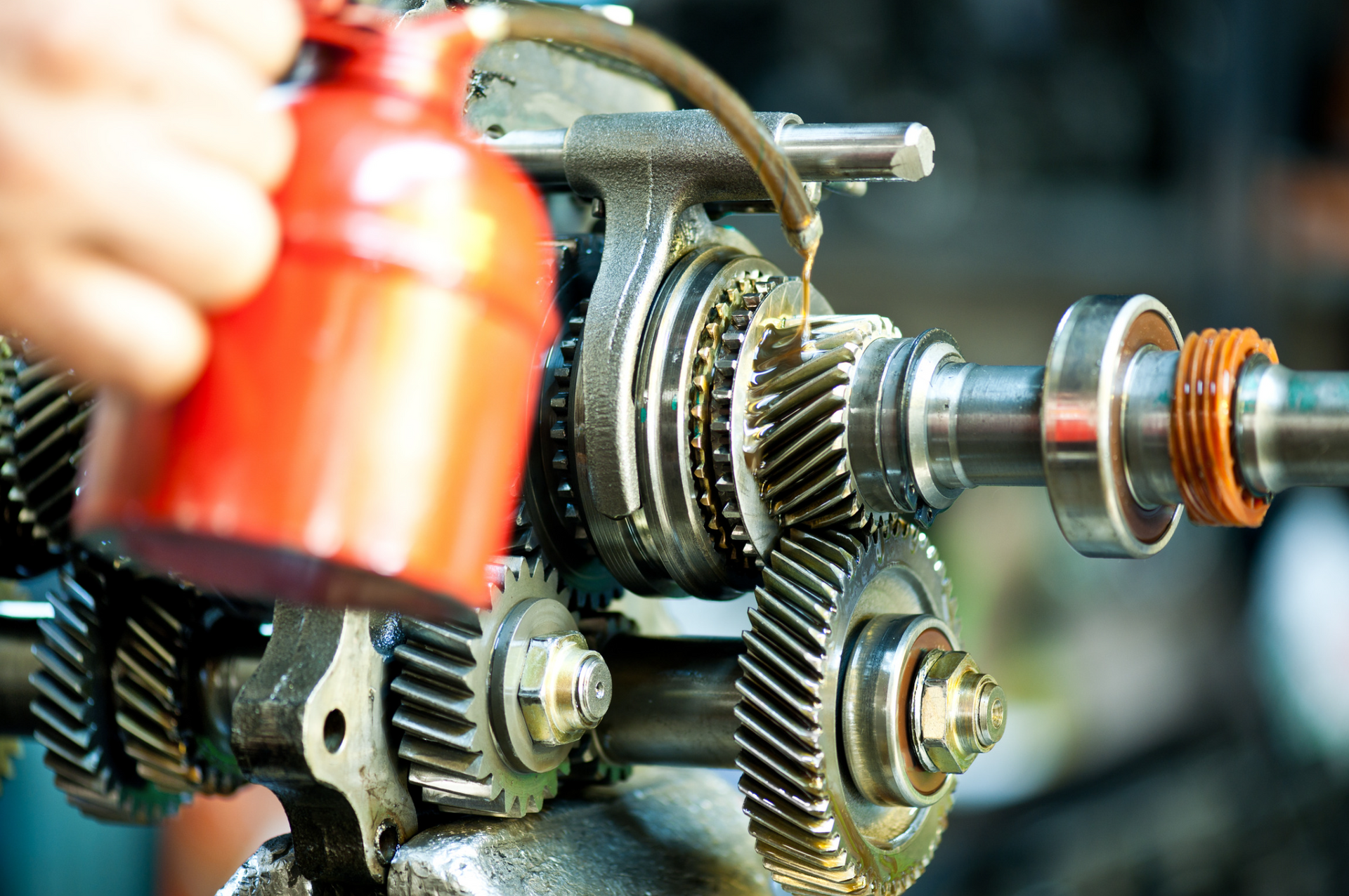 A person is holding a red oil can over a gearbox.