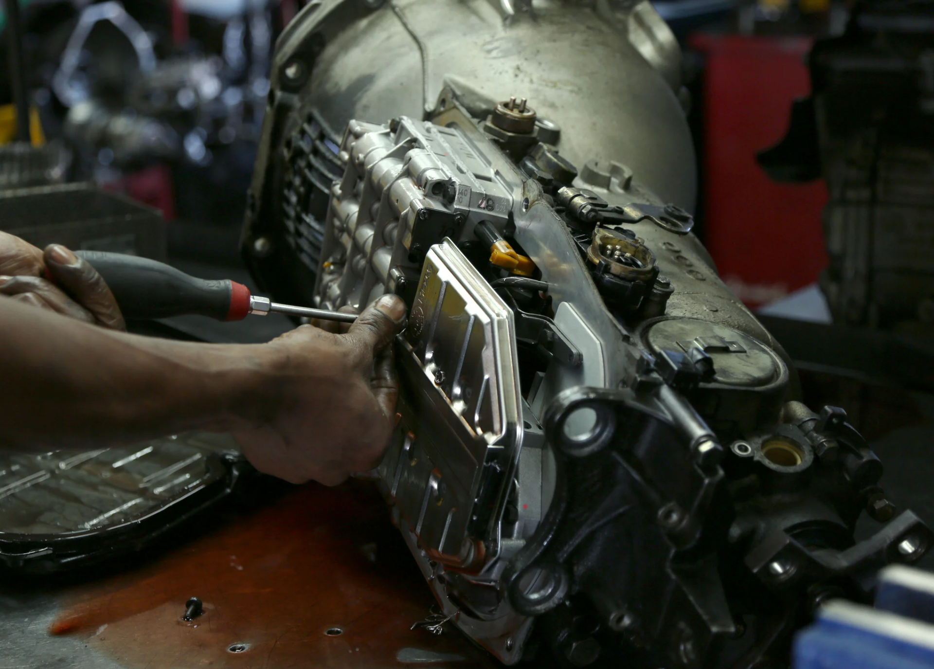 A man is working on a car engine with a screwdriver.
