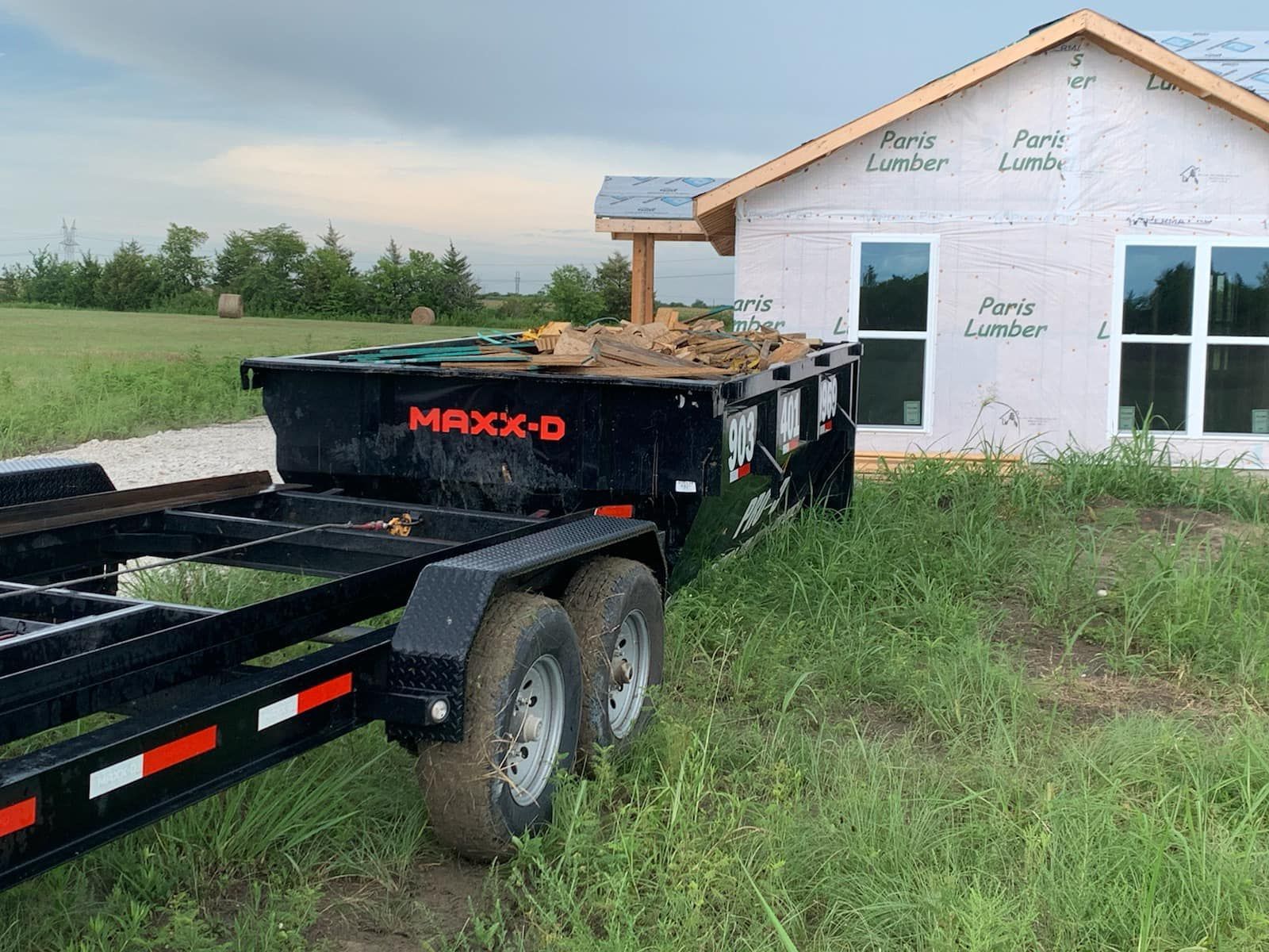 A black MAXX-D dumpster trailer partially filled with construction debris
