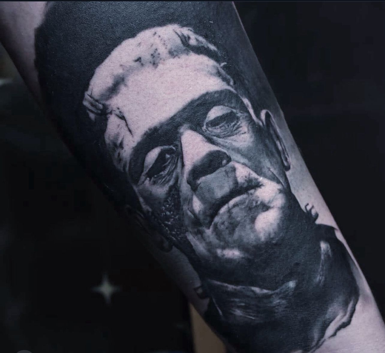 Black-and-grey tattoo of Frankenstein’s monster, focusing on the character's somber expression and textured facial skin.