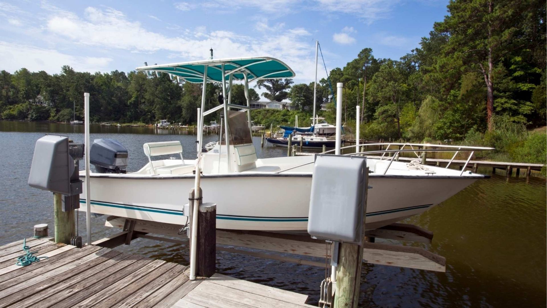 White boat on a lift at a dock, green canopy, trees in the background, sunny day.