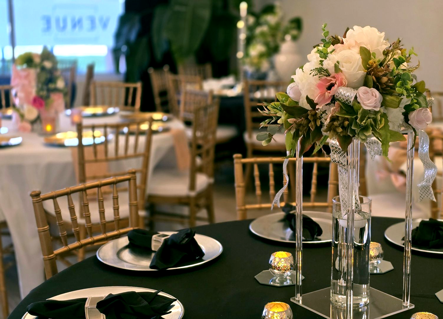 Elegant event table setting with floral centerpiece, gold chairs, and black tablecloth.