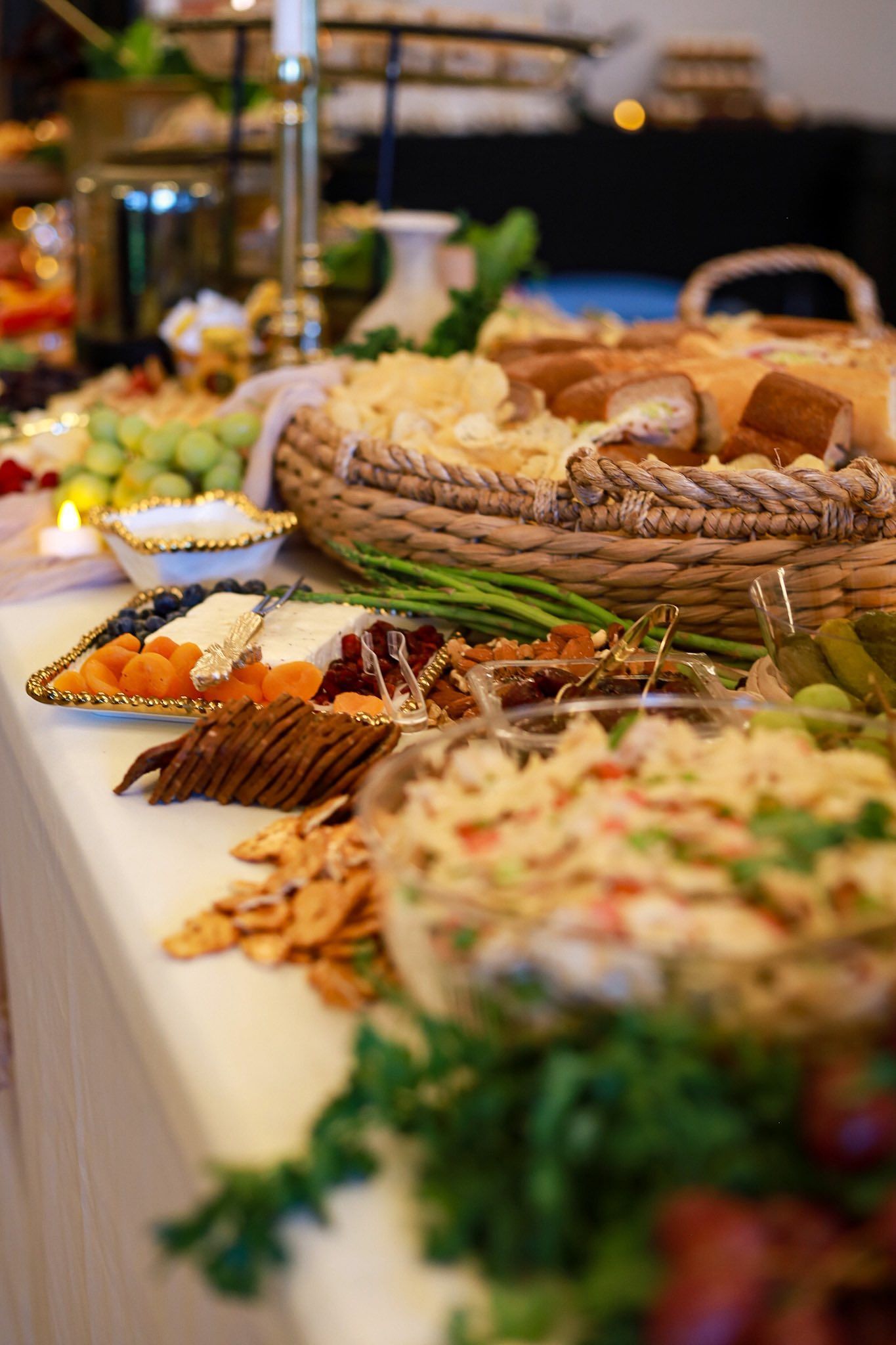 Charcuterie Buffet table with assorted foods: cheese, crackers, bread, fruit, dips, and green garnishes.