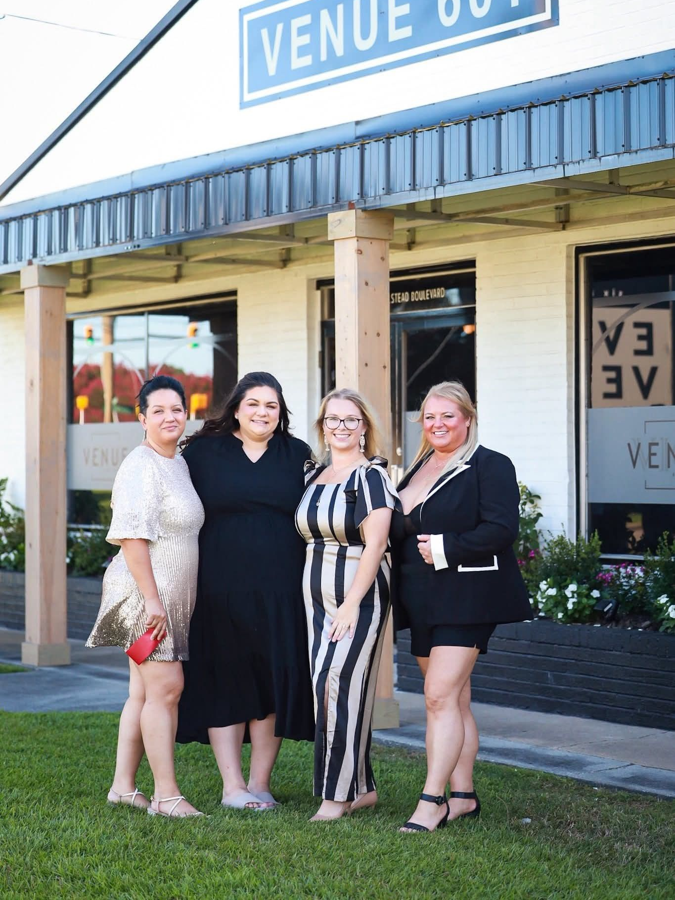 Four women pose outside a venue. The women are smiling, and the building has a blue sign.
