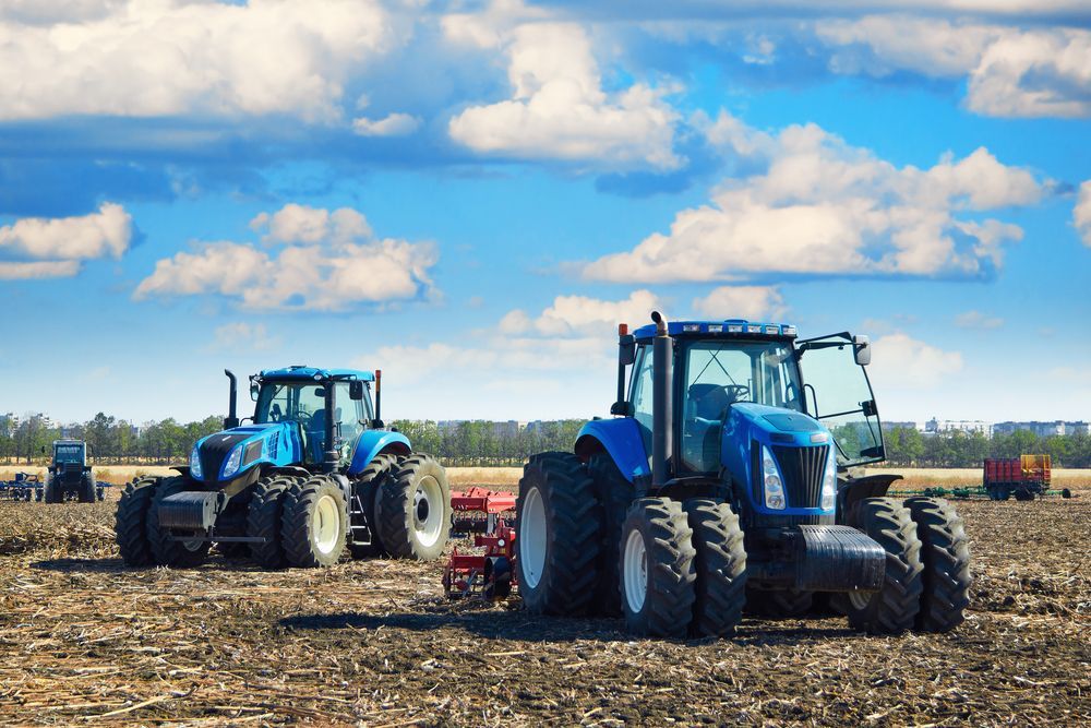 Two Blue Tractors Are Plowing A Field On A Sunny Day — Fewmore Contracting In Tennant Creek, NT