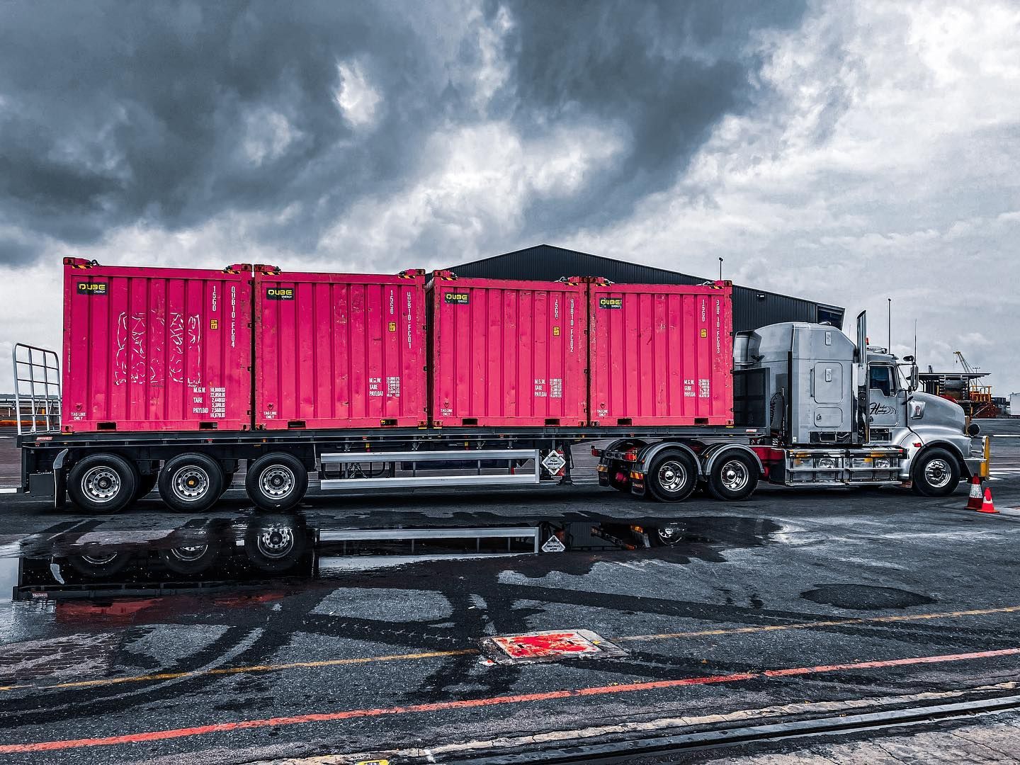A Semi Truck is Carrying Pink Shipping Containers on a Wet Road — Fewmore Contracting in Yarrawonga, NT