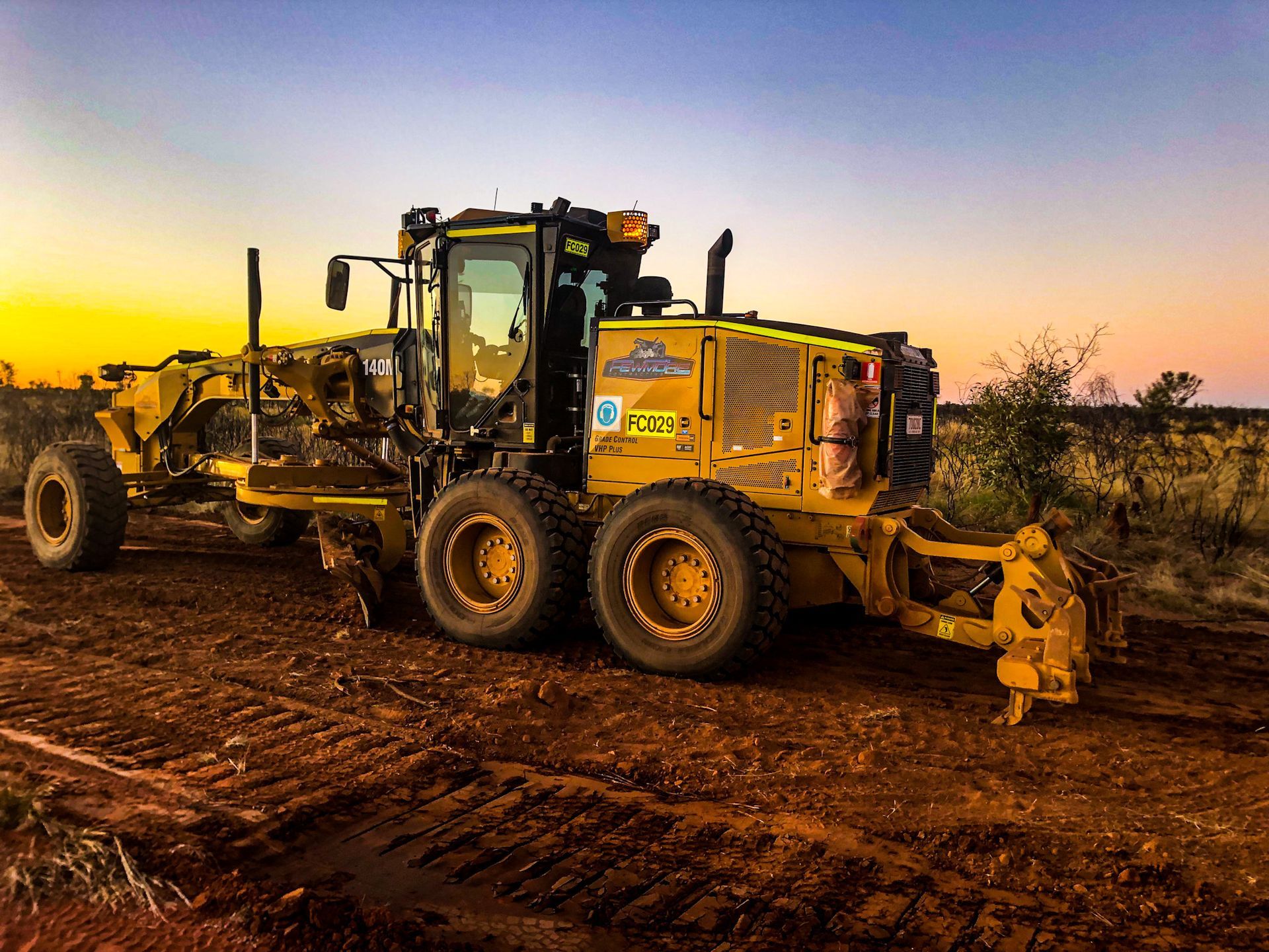 A Yellow Tractor is Parked on a Dirt Road at Sunset — Fewmore Contracting in Yarrawonga, NT