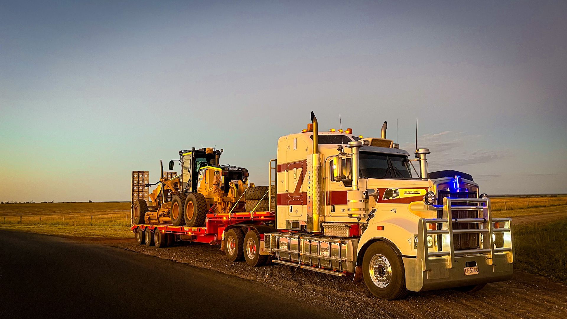 A Semi Truck is Carrying a Bulldozer Down a Dirt Road — Fewmore Contracting in Yarrawonga, NT