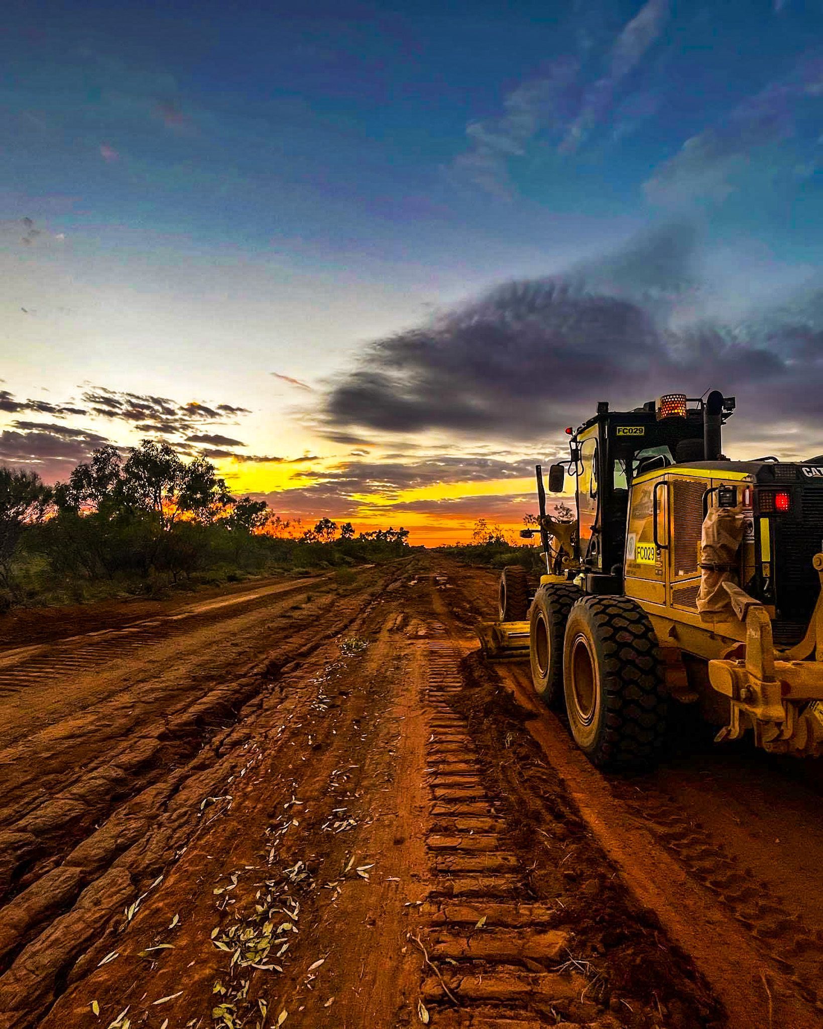 A Bulldozer is Driving Down a Dirt Road at Sunset — Fewmore Contracting in Yarrawonga, NT