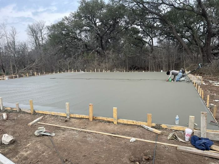 Workers in high-visibility vests smooth freshly poured concrete for a residential driveway.