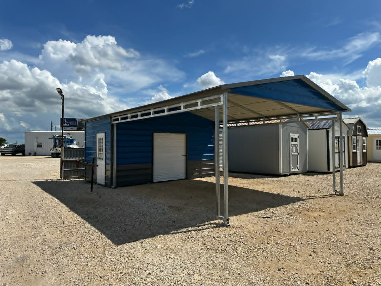 Blue shipping container and metal canopy in a gravel lot under a sunny sky