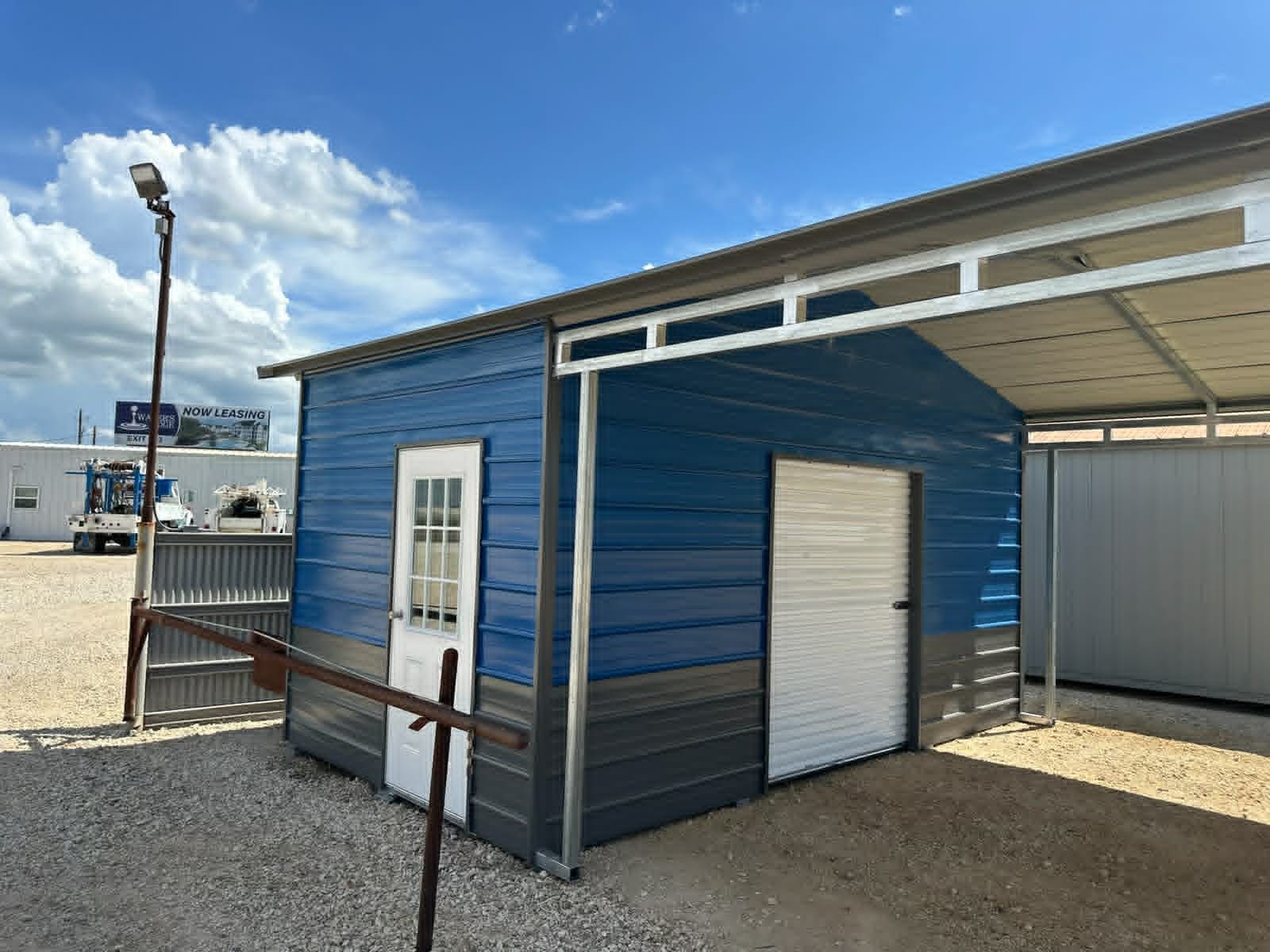 Blue kiosk with white doors and a metal awning on a sandy outdoor lot