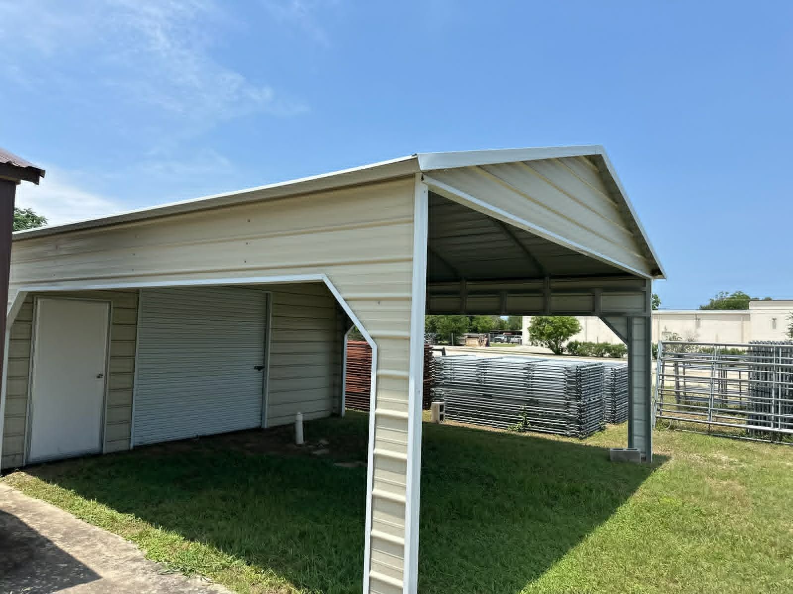 White metal carport with a gabled roof over grass beside a house on a sunny day