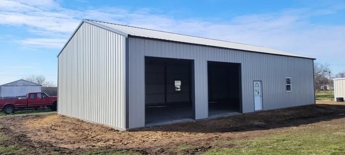 Gray metal garage building with two open bays and a side door on a dirt lot