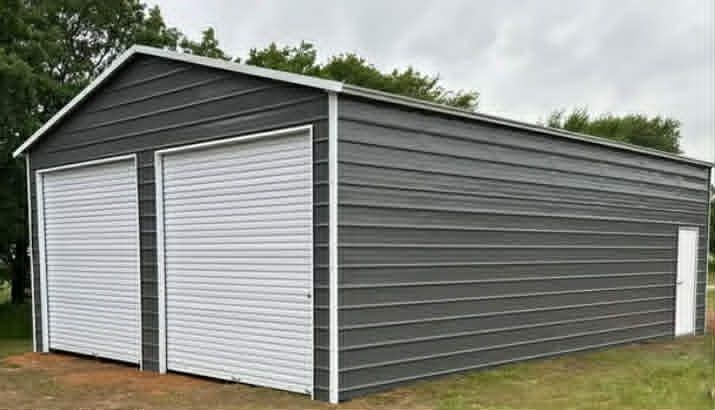 Gray metal storage shed with two white roll-up doors and a side entry door on grass