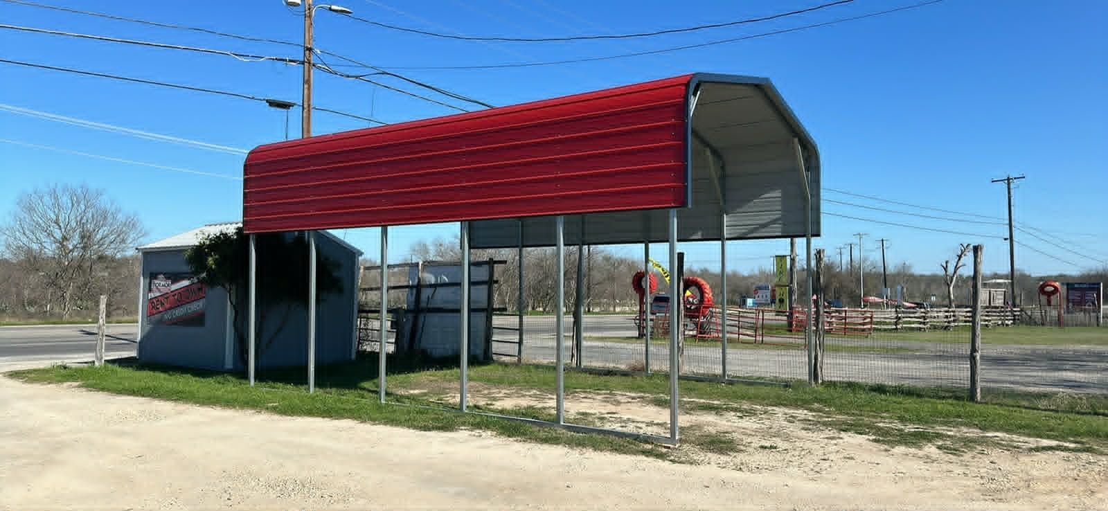 Red-roofed bus stop shelter beside a fenced outdoor recreation area under a blue sky