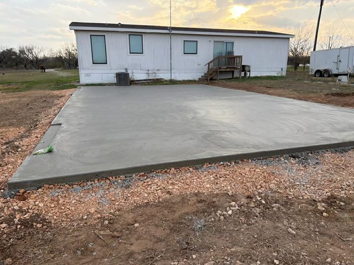 A worker in a high-visibility vest guides wet concrete from a mixer truck into a large metal hopper at a construction site.