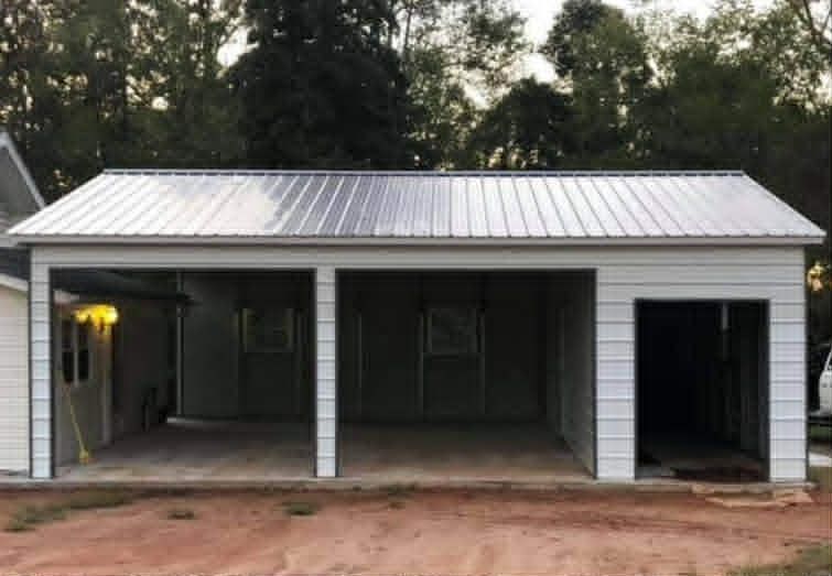 Three-bay metal carport with white siding and lit porch light in front of trees