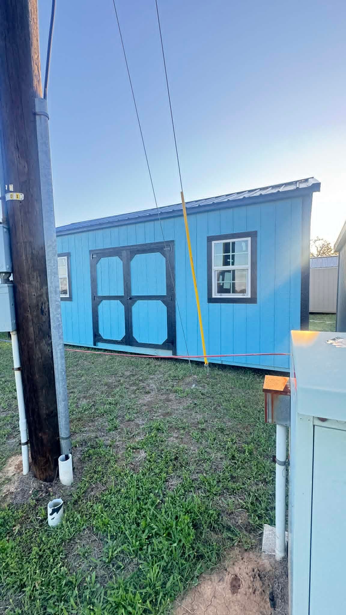 Blue tiny house with black-trimmed double doors beside a utility pole in a grassy yard.