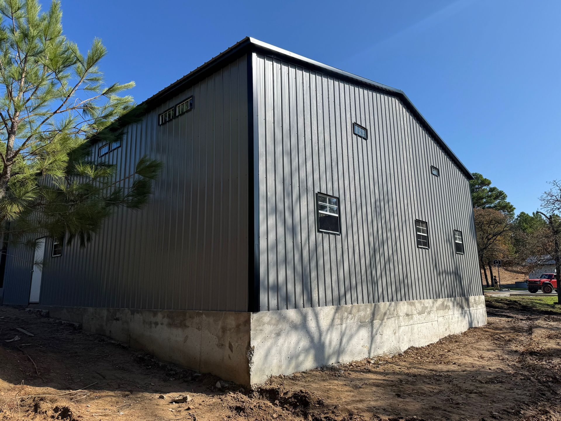 Gray metal barn or shed with a concrete foundation, seen from the side under a blue sky.