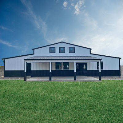 White barn-style building with black trim and a covered porch, set behind a green lawn under a blue sky