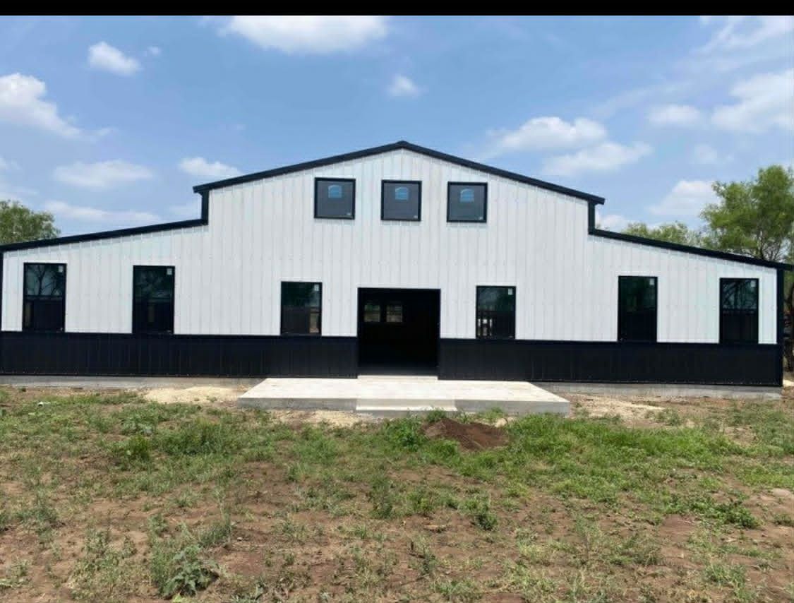 White and black metal building with a covered porch on a dirt lot under a cloudy sky
