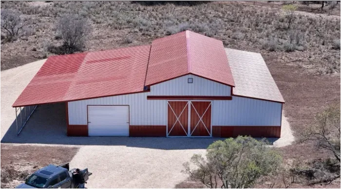 Aerial view of a red-roofed barn and garage in a dry rural landscape, with a car parked nearby
