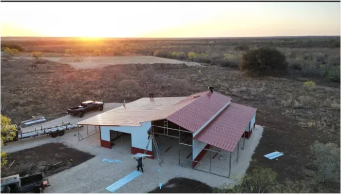 Sunset over a red-roofed house under construction in a dry, open landscape