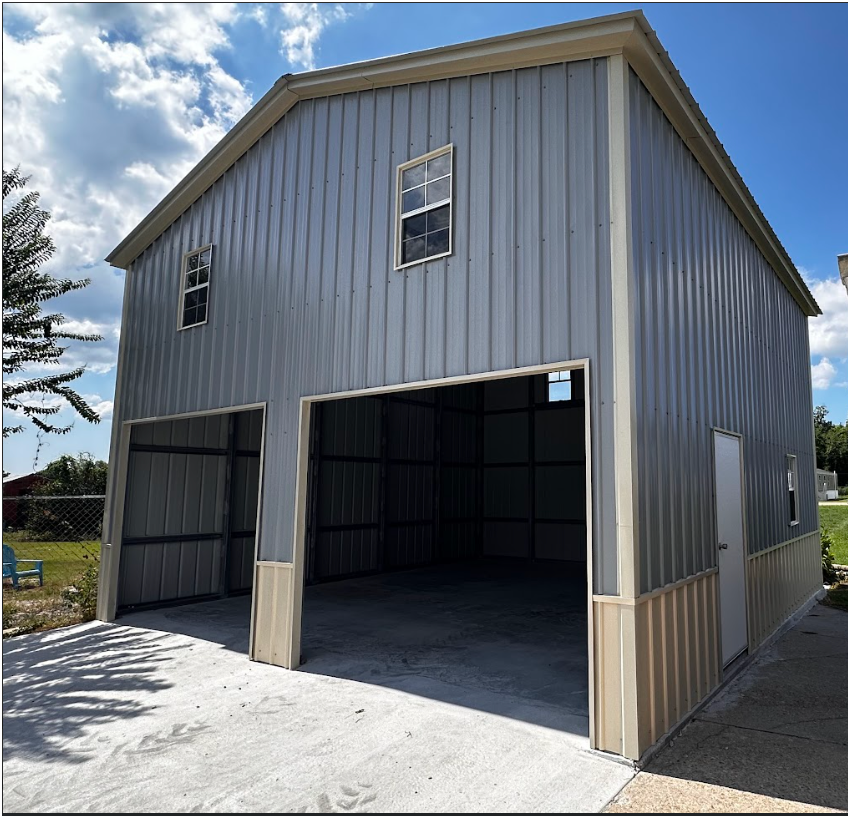 A two-story, grey metal garage with two large openings, a single white side door, and two upper-level windows.