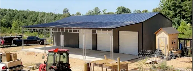 Large barn-style building with dark siding and white garage doors under construction on a rural site