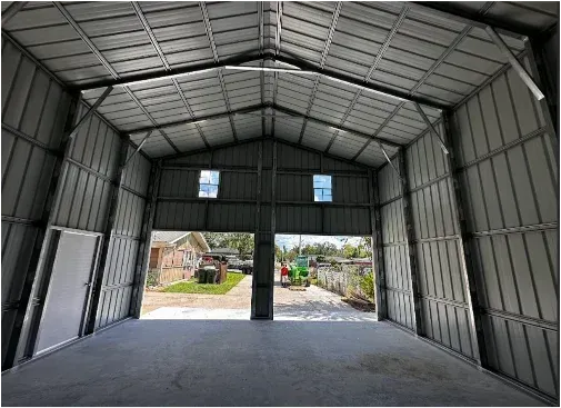 Interior of a large metal warehouse with open front and dirt floor, looking out to a yard beyond.