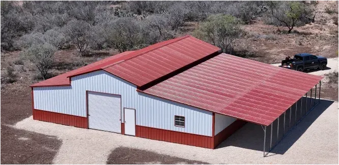 Aerial view of a white barn with red metal roofs in a dry, wooded area