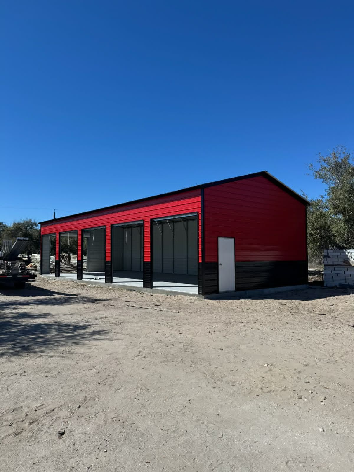 Red commercial building with black trim and large windows on a gravel lot under a clear blue sky