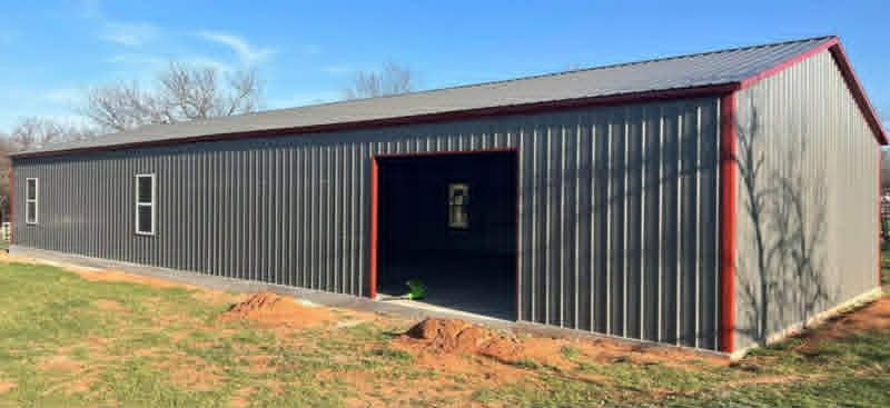 Long black metal barn with red trim and open front door on a grassy lot