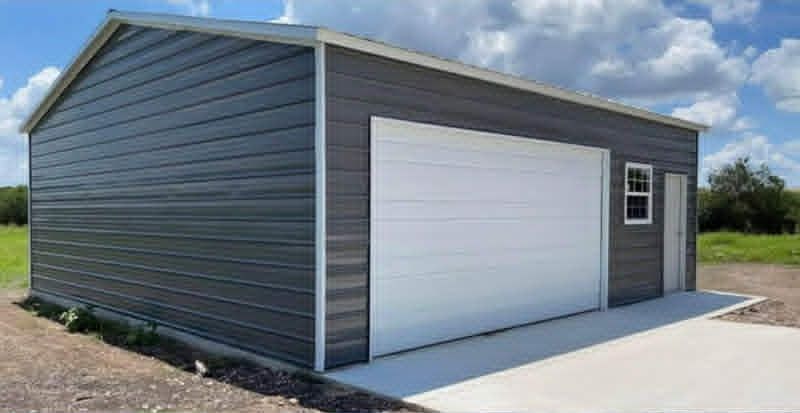 Gray metal garage with a white roll-up door and side entry door under a blue sky