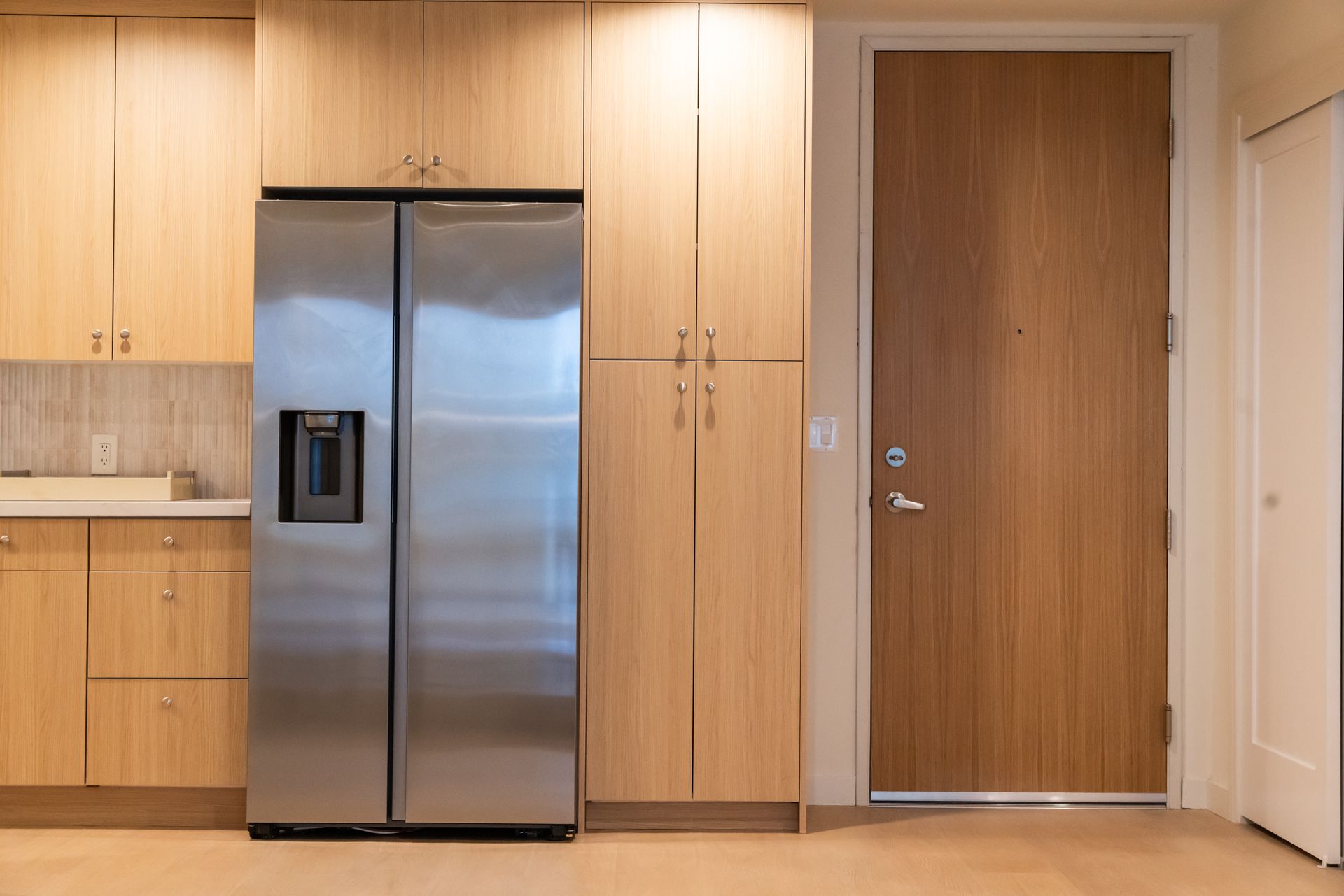 Kitchen with stainless steel refrigerator, wooden cabinets, and a wooden entry door.