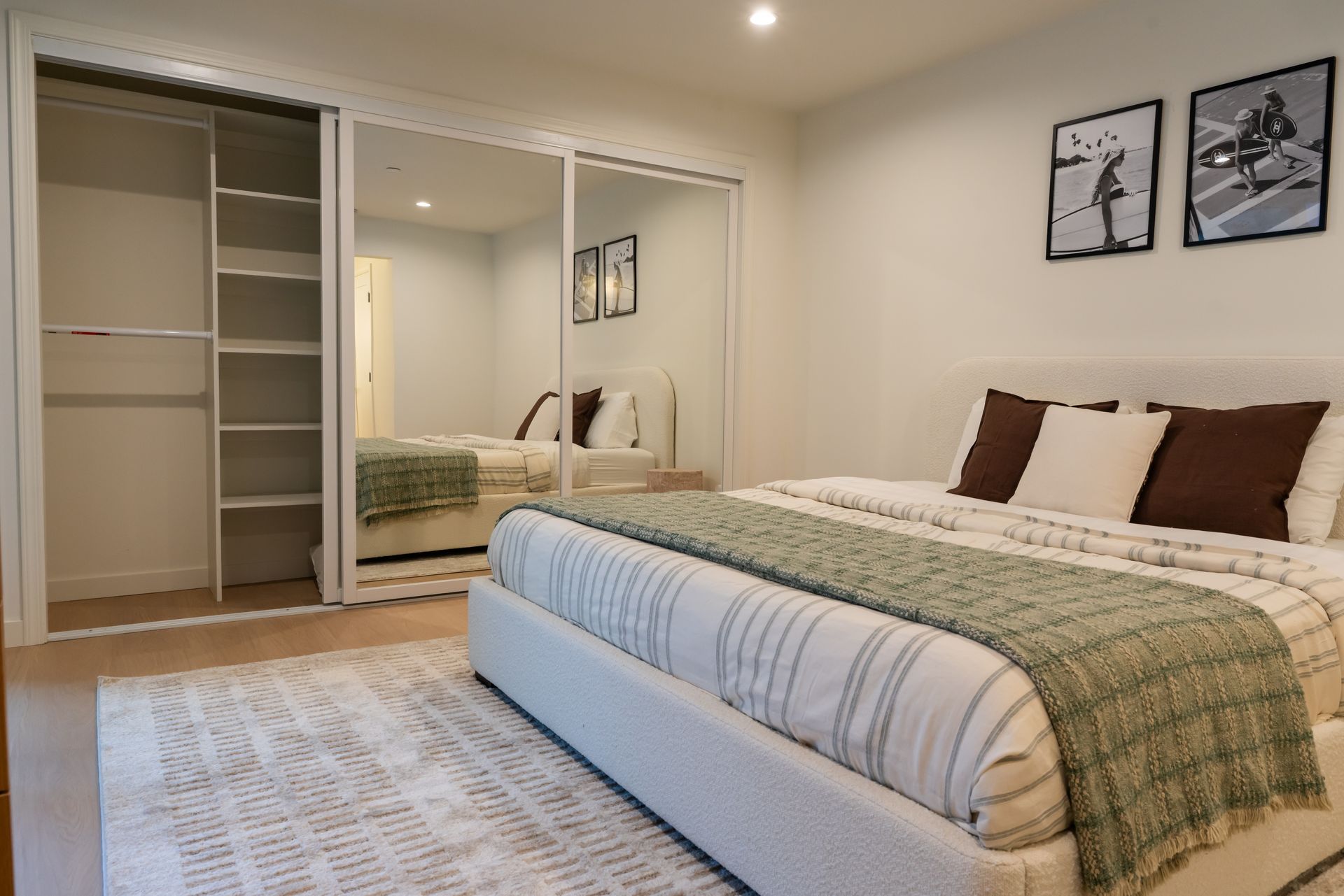 Bedroom with a bed, closet, and mirrored sliding doors. Green and brown accents. Artwork on the wall.