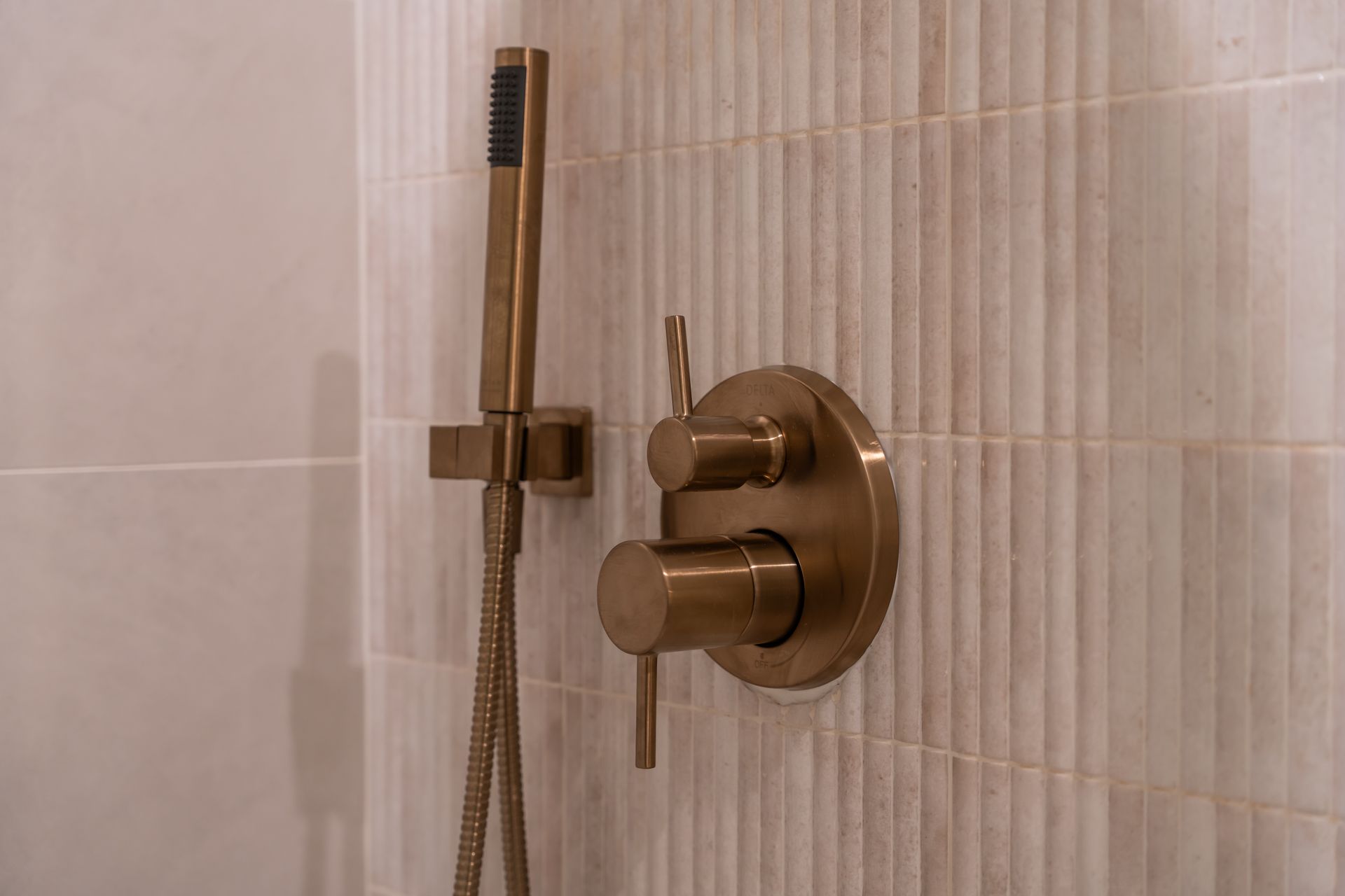 Bronze shower fixtures mounted on textured, cream-colored tile.