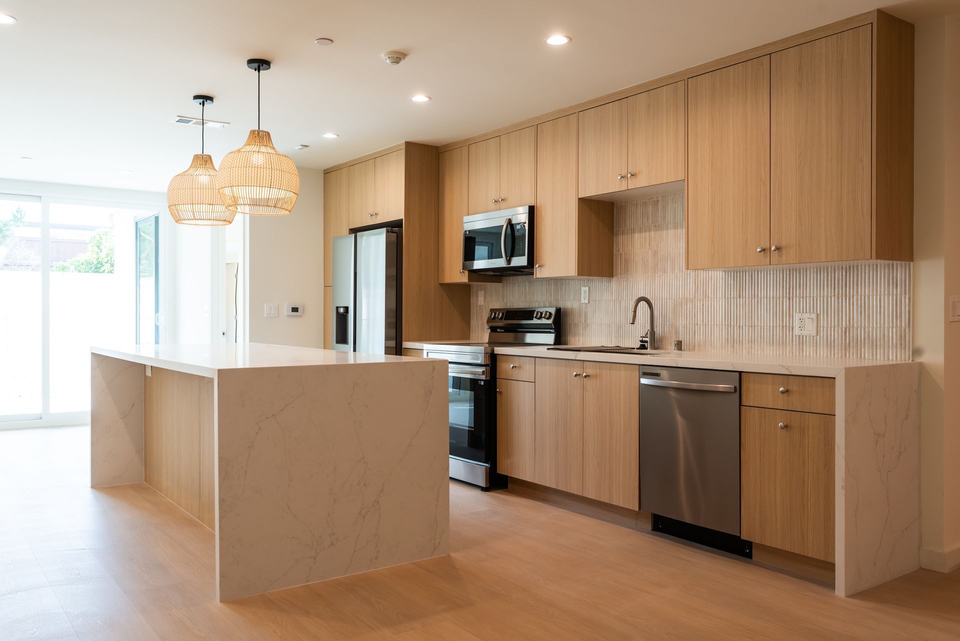 Modern kitchen with light wood cabinets, stainless steel appliances, and a quartz island.