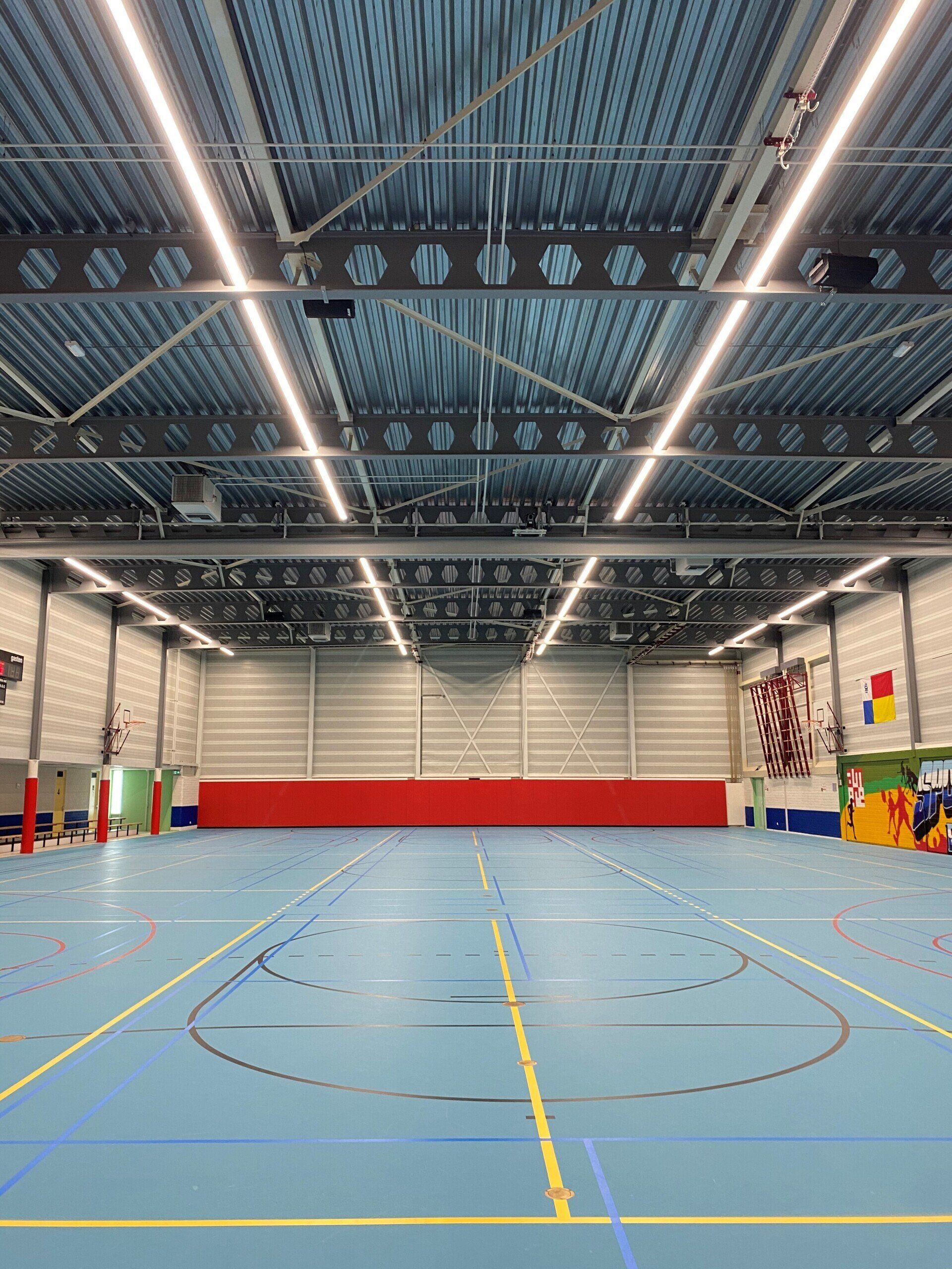 Een groot indoor basketbalveld met een blauwe vloer en een rode muur.