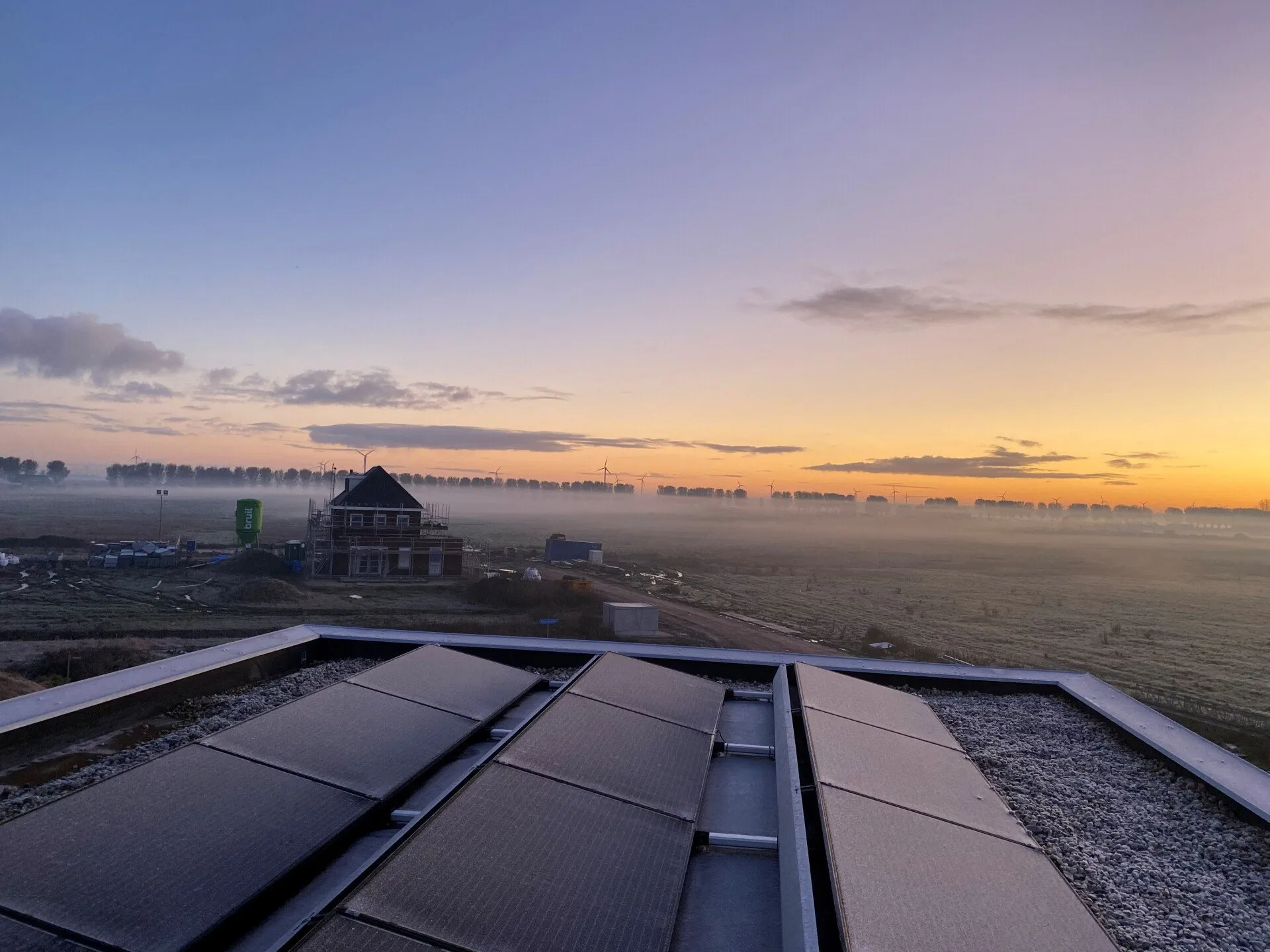 Een rij zonnepanelen op een dak bij zonsondergang