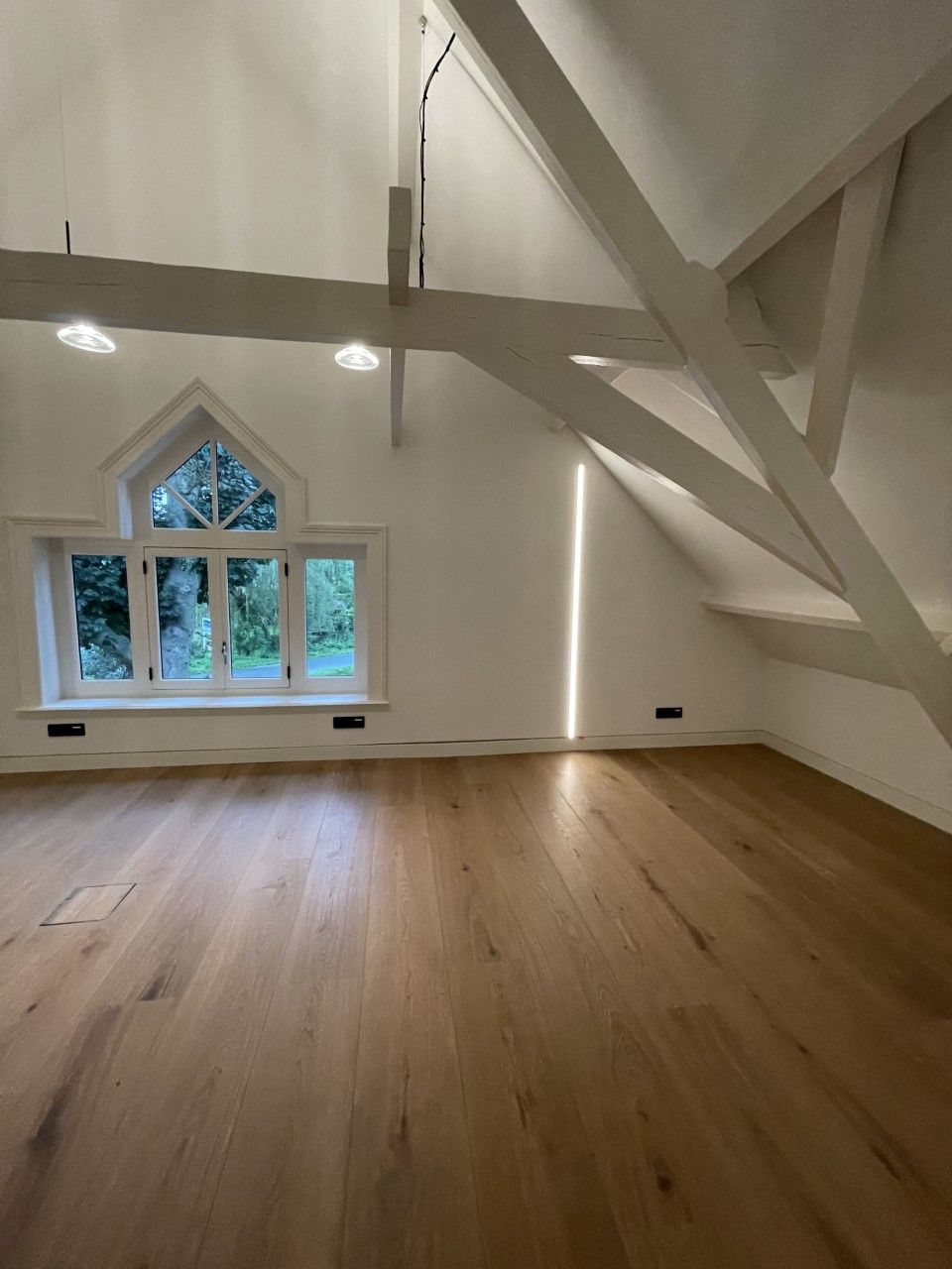 Een lege kamer met een houten vloer en een groot raam lampen aan het plafond
