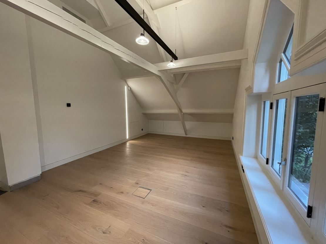 Een grote lege kamer met hardhouten vloeren en witte muren. en verlichting