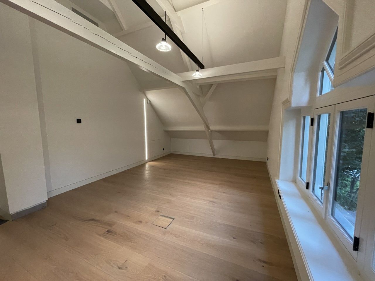 Een grote lege kamer met hardhouten vloeren en witte muren. en verlichting