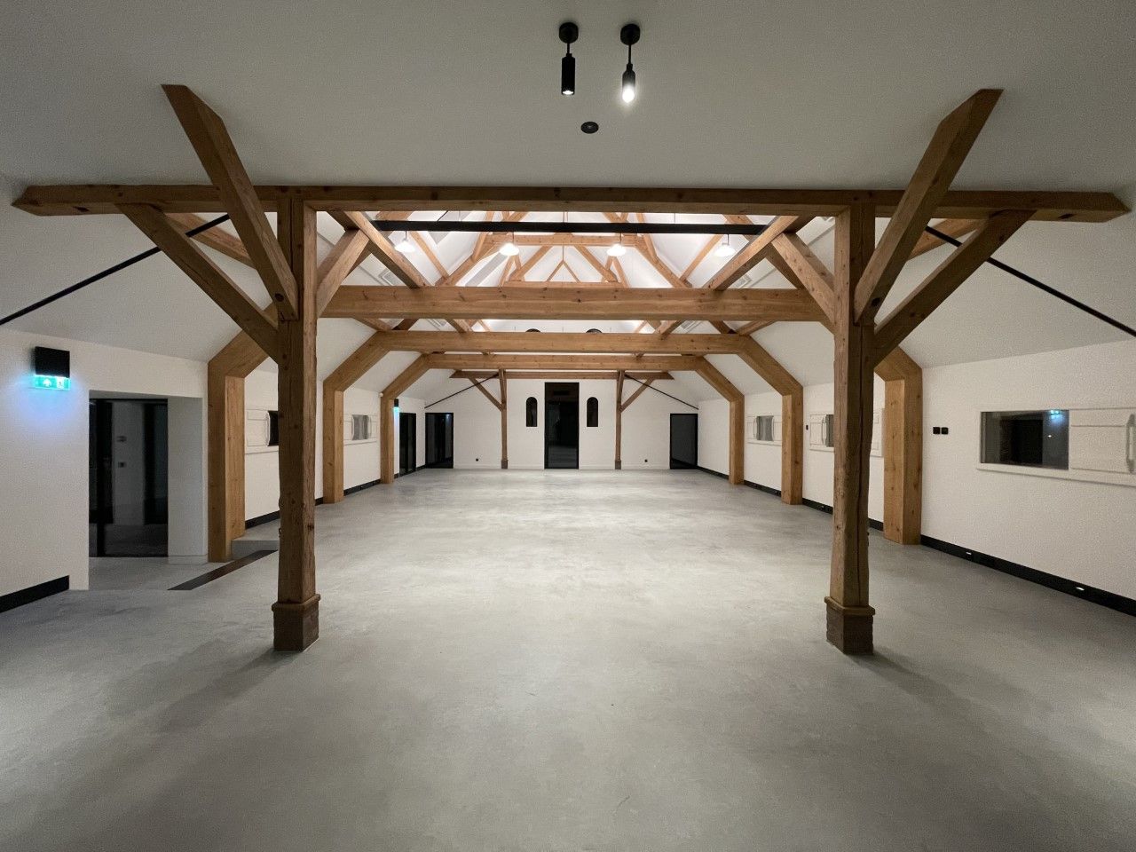 Een grote lege kamer met houten balken en witte muren en verlichting aan het plafond